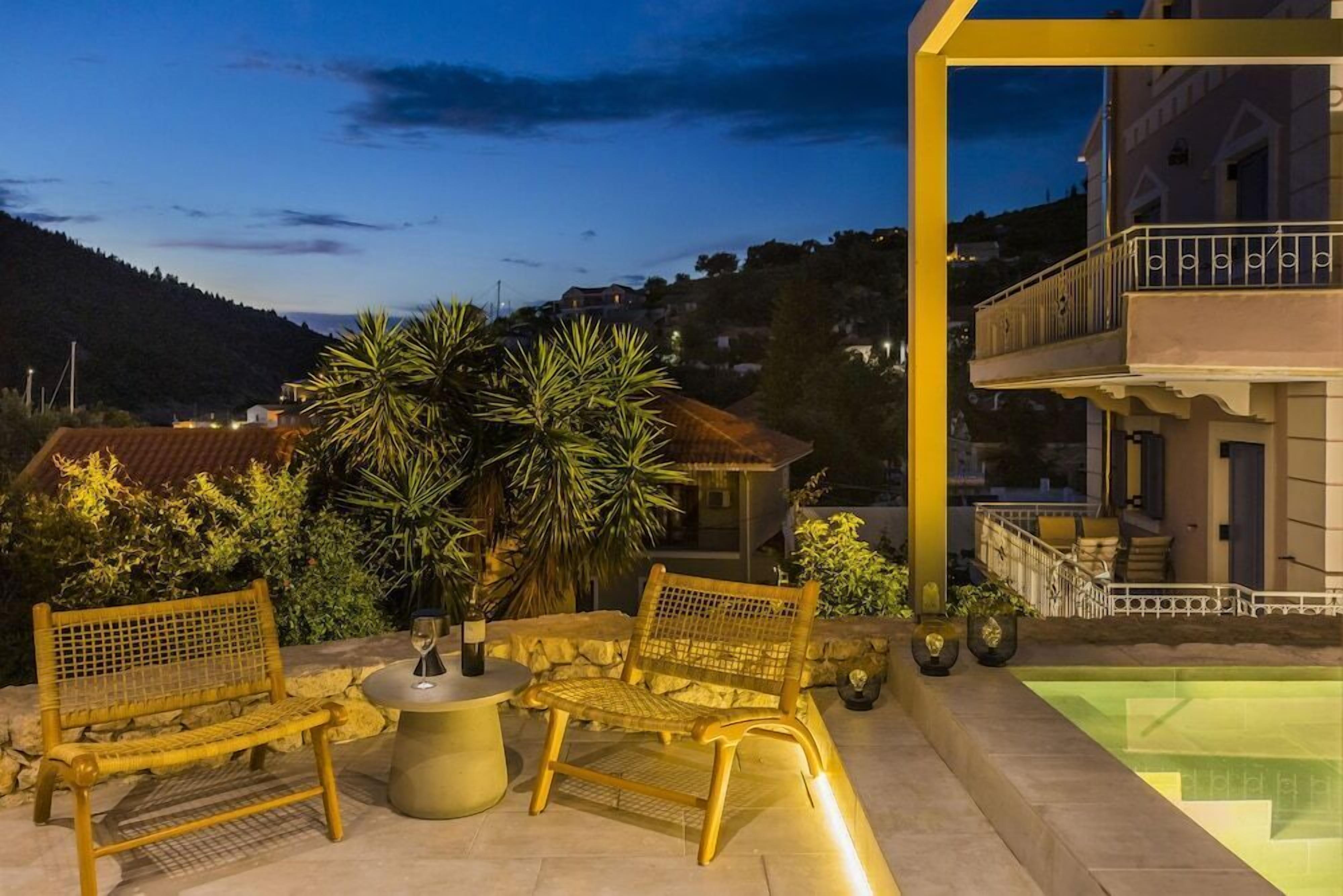 An outdoor seating area with two wicker chairs and a table, a pool, and a building with a balcony.