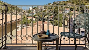 A balcony with a view of a hillside town, a table with a vase and a bowl, and a chair. - Chromata Assos Villas Kefalonia (Kefalonia)
