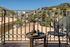 Un balcón con vistas a un pueblo en la ladera, una mesa con un florero y un cuenco, y una silla.