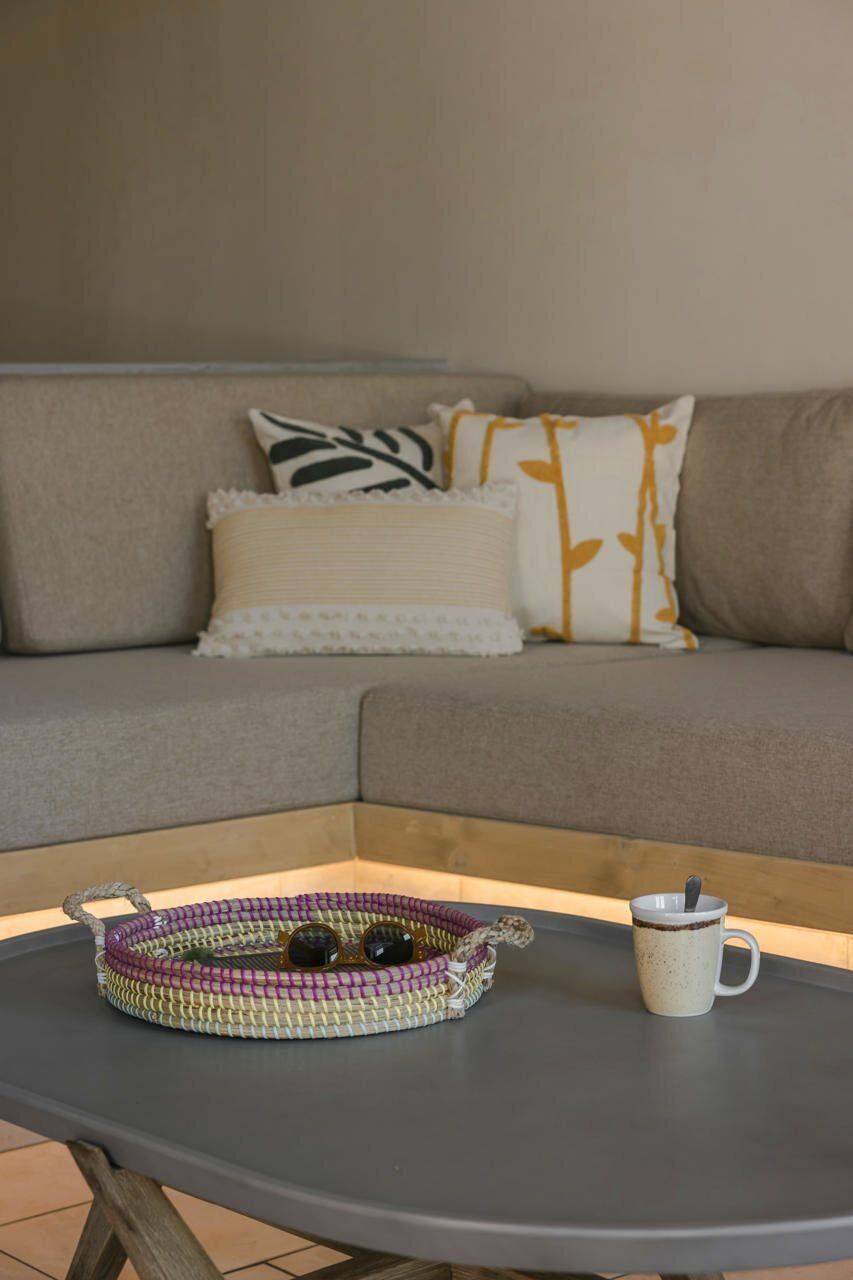 A grey sofa with patterned cushions, a woven tray with sunglasses and a mug, and a small table in front.