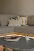 A grey sofa with patterned cushions, a woven tray with sunglasses and a mug, and a small table in front.