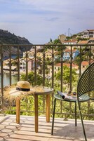 Un balcón con vistas a un pueblo costero, un sombrero de paja y una silla.