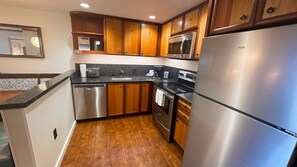 A kitchen with wooden cabinets, stainless steel appliances, and a black countertop. - Ko Olina | Disney Family Adventure | Lagoon + Pool | 3BR Sleeps 12 (Kapolei)