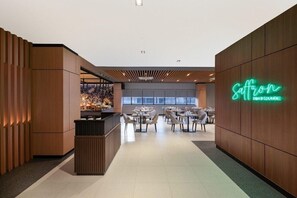 Un interior moderno con un letrero de neón que dice 'Saffron Dining Lounge', con una zona de recepción y mesas de comedor.