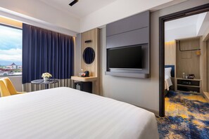 Habitación de hotel con una cama grande, un televisor montado en la pared, una mesita con un jarrón de flores y vistas al exterior.