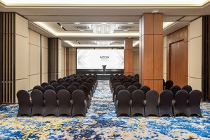 A conference room with rows of chairs facing a presentation screen, a carpeted floor, and a modern ceiling design. - Aston Malang Hotel and Conference Center (Malang)