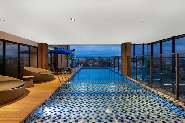 Una piscina infinita en la azotea con piso a cuadros, asientos de madera y vistas a la ciudad.