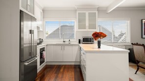 A modern kitchen with white cabinetry, stainless steel appliances, and a wooden floor. - The Leafy Outlook Family Stay in Randwick (Randwick)