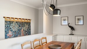 A dining area with a wooden table, chairs, a tapestry, and wall-mounted artwork. - The Leafy Outlook Family Stay in Randwick (Randwick)