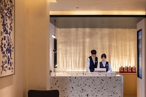 A reception desk with two staff members, a wall with abstract art, and a window with curtains. - Chengdu Tianfu Square Chunxi Road Pagoda Premium Hotel (Chengdu)