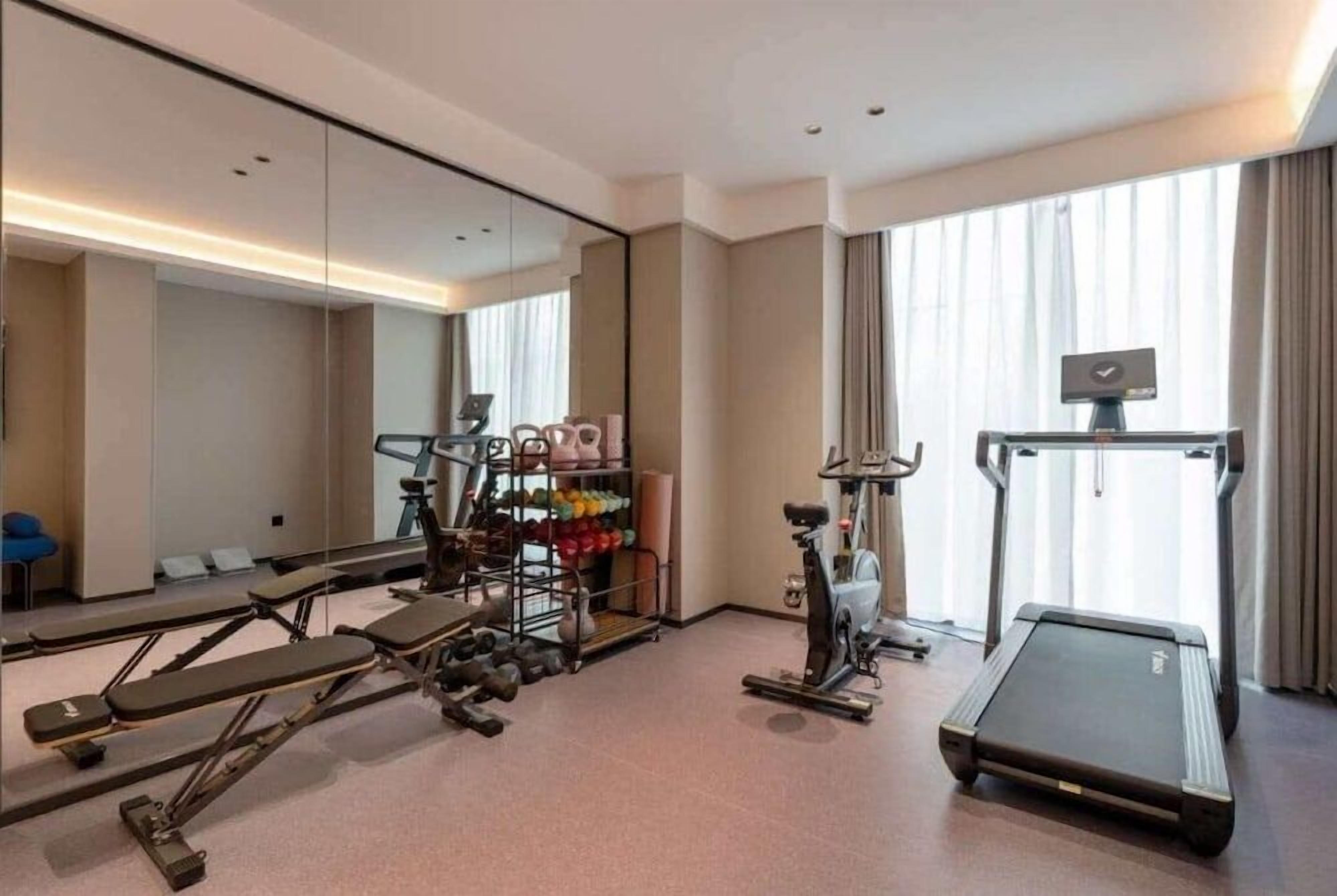 A hotel room with a gym area including a treadmill, exercise bike, and weight bench.