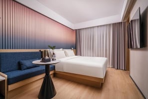Une chambre d’hôtel avec un lit, un canapé bleu, une petite table avec une lampe et un téléviseur fixé au mur.
