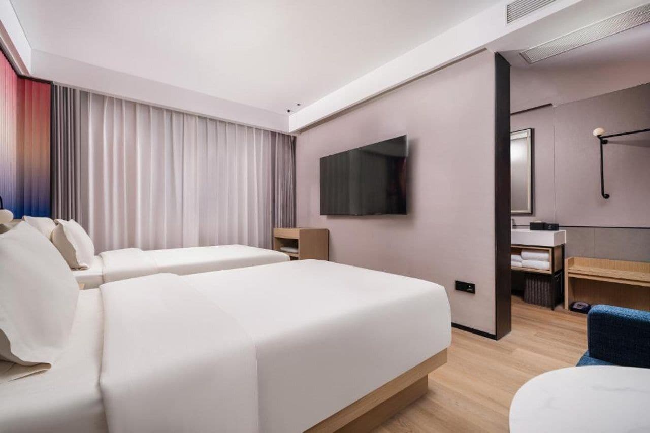 A hotel room with two beds, a TV, a desk, and a bathroom.