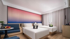 Een hotelkamer met twee bedden, een bank, een kleine tafel, en een panda-knuffel op elk bed.