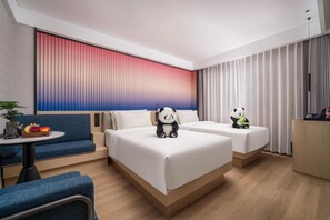 Habitación de hotel con dos camas, un sofá, una mesita y un peluche de panda sobre cada cama.