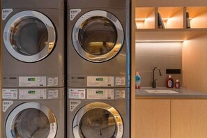 A stack of four front-loading washing machines with control panels, a sink, and a shelf with books. - Chengdu Tianfu Square Chunxi Road Pagoda Premium Hotel (Chengdu)