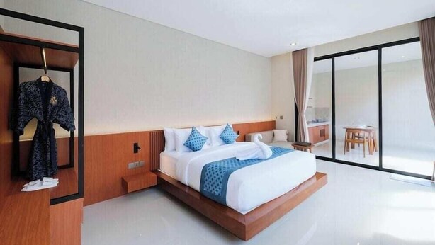 Una habitación de hotel moderna con una cama grande, una mesita de noche de madera, un espejo y vistas al exterior por una puerta de cristal corredera.
