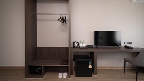 Habitación de hotel compacta con cama, escritorio con televisor, mini refrigerador y zapatero.