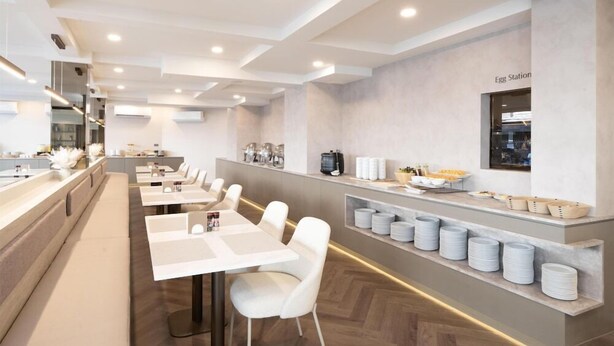 A modern dining area with white tables and chairs, a counter with food items, and a wall-mounted sign. - Surestay Plus by Best Western Ramkhamhaeng Airport Rail Link Bangkok (Bangkok)
