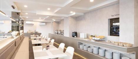 A modern dining area with white tables and chairs, a counter with food items, and a wall-mounted sign.