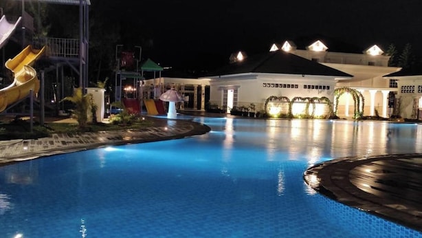A nighttime swimming pool area with a slide and a building in the background. - Beth Kasegaran Theresia (Megamendung)