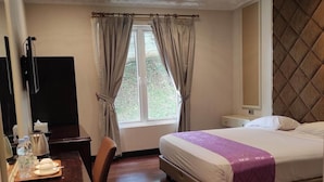 A hotel room with a bed, a desk, a chair, a TV, and a window with curtains. - Beth Kasegaran Theresia (Megamendung)
