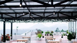 An outdoor terrace with tables and chairs, potted plants, and a view of the mountains. - Beth Kasegaran Theresia (Megamendung)