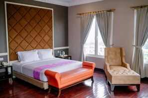 A hotel room with a bed, a chair, a nightstand, and a window with curtains. - Beth Kasegaran Theresia (Megamendung)