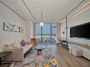 A modern hotel room with a sofa, a coffee table, a TV, and a large window offering a view of the airport. - Hilton Garden Inn Guangzhou Baiyun Airport (Guangzhou)