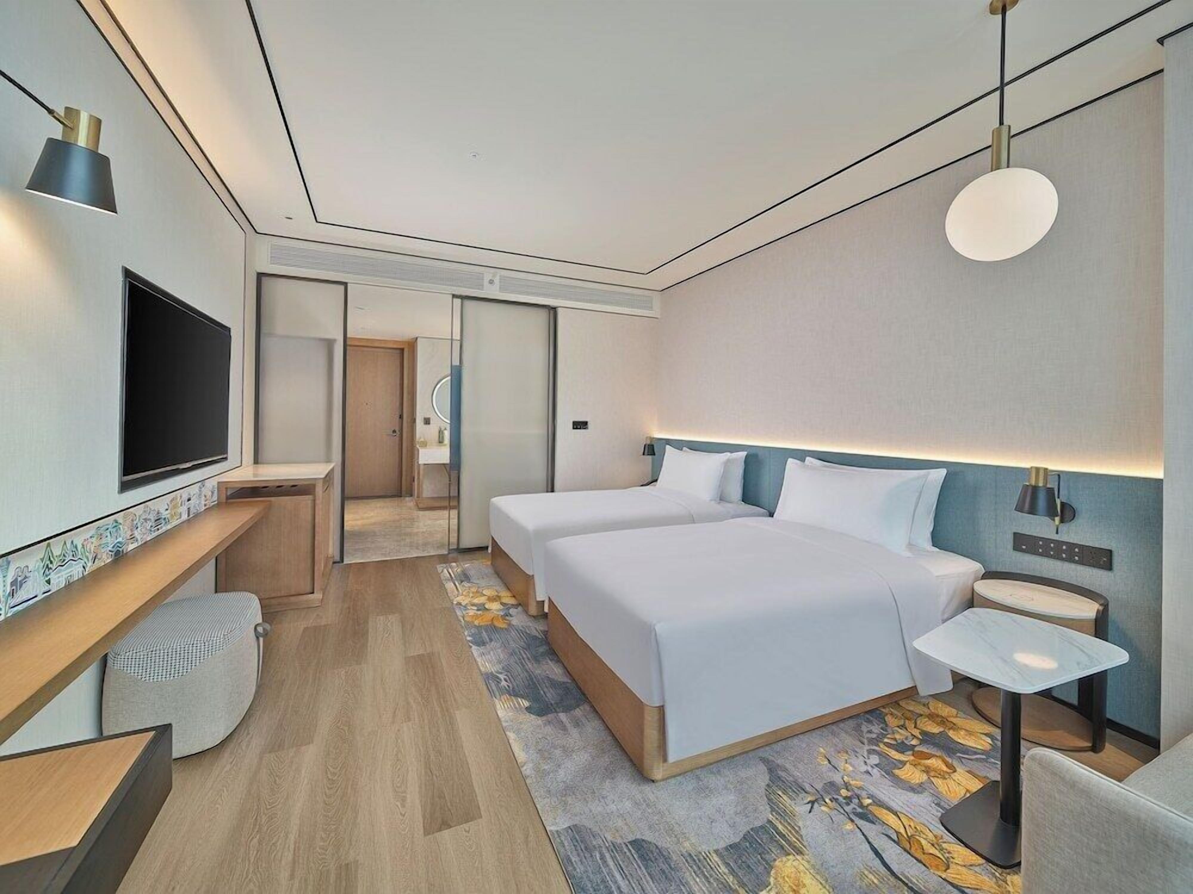 A modern hotel room with a large bed, bedside tables, a TV, and a small seating area.