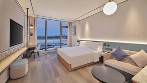 A modern hotel room with a large bed, a sofa, a desk, and a TV. - Hilton Garden Inn Guangzhou Baiyun Airport (Guangzhou)