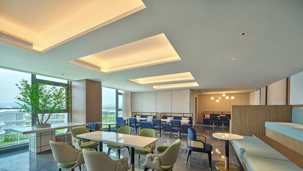 A modern interior with a dining area, seating, and a view through large windows. - Hilton Garden Inn Guangzhou Baiyun Airport (Guangzhou)