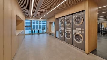 Une buanderie moderne équipée de plusieurs machines à laver, avec un lambris en bois et une vue sur l’extérieur grâce à de grandes fenêtres.