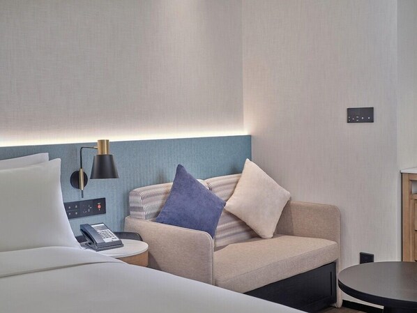 A modern hotel room with a sofa, a bedside table with a phone, a lamp, and a small round table. - Hilton Garden Inn Guangzhou Baiyun Airport (Guangzhou)