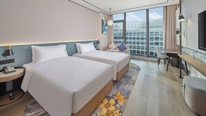 A hotel room with two beds, a desk, a chair, a small table, a lamp, and a large window with a city view. - Hilton Garden Inn Guangzhou Baiyun Airport (Guangzhou)