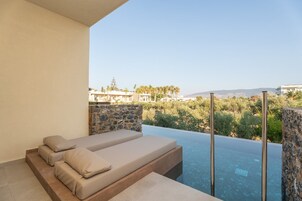 Un balcón con pared de piedra, una zona de estar con cojines y una piscina con vistas despejadas del paisaje circundante.