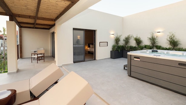 A modern outdoor living area with a hot tub, seating, and a sliding glass door leading to a bedroom. - Arato by E.geo (Kos)