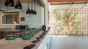 A kitchen with a long counter, multiple pots, a microwave, and hanging lights. - Arato by E.geo (Kos)