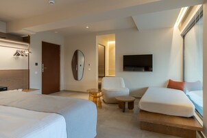 Habitación de hotel con dos camas, un espacio para sentarse con una silla y una mesita, un espejo, un televisor y un armario.