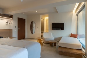 Habitación de hotel con dos camas, un espacio para sentarse con una silla y una mesita, un espejo, un televisor y un armario.