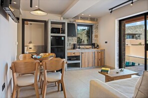 A modern kitchen with stone accents, a dining area with wooden furniture, and a view of a pool. - Volta Seaside Hotel - Adult-only (Hersonissos)