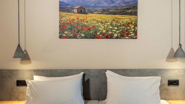 Ein Doppelbett mit zwei Kissen und einer Decke, ein Gemälde von einem Feld mit Blumen und Bergen sowie zwei Pendelleuchten.