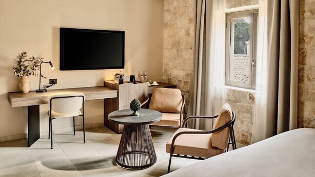 Une chambre d’hôtel équipée d’un téléviseur à écran plat, d’un bureau, de deux chaises, d’une table ronde et d’un lit.