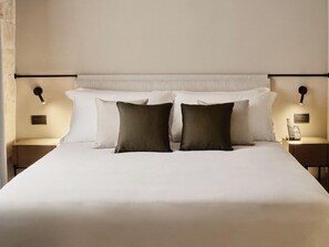 A neatly made bed with white and dark pillows, two bedside tables with lamps, and a wall-mounted light fixture. - Costa Borgo Ragusa (Ragusa)
