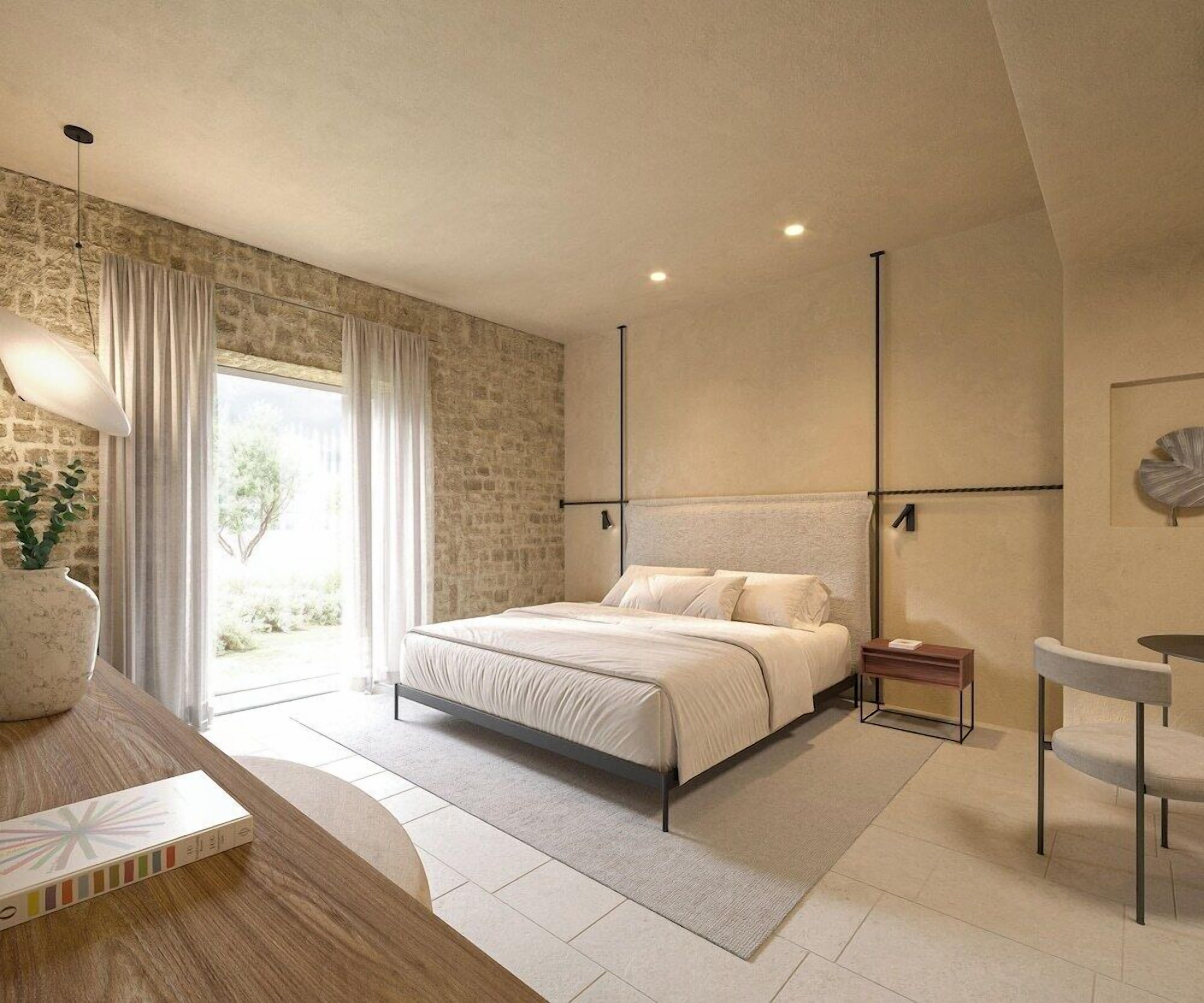 A modern bedroom with a large bed, a bedside table, a nightstand, a window with curtains, and a stone wall.