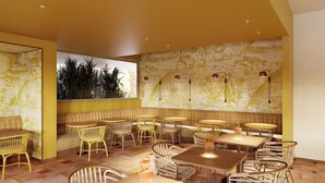 L’intérieur d’un restaurant aux couleurs dominantes jaunes, avec des meubles en osier et un papier peint à motifs.