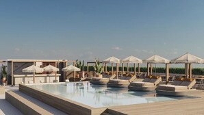 Un espace piscine aménagé sur le toit, avec des chaises longues et des parasols, entouré de verdure et surplombant un ciel dégagé.