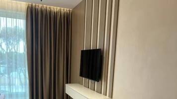 A modern living room with a sofa, a flat-screen TV mounted on a wall, and a window with curtains.