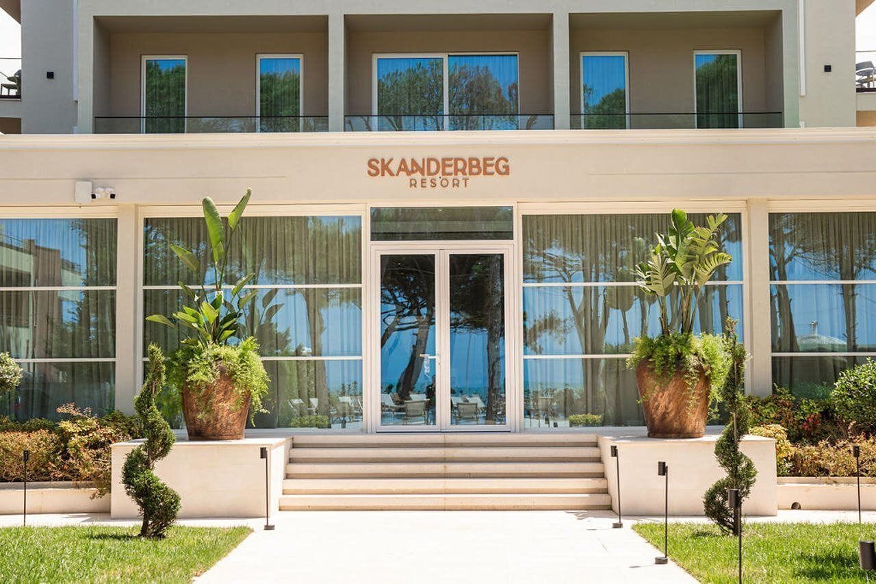 A modern hotel entrance with a double door, large windows, and potted plants.