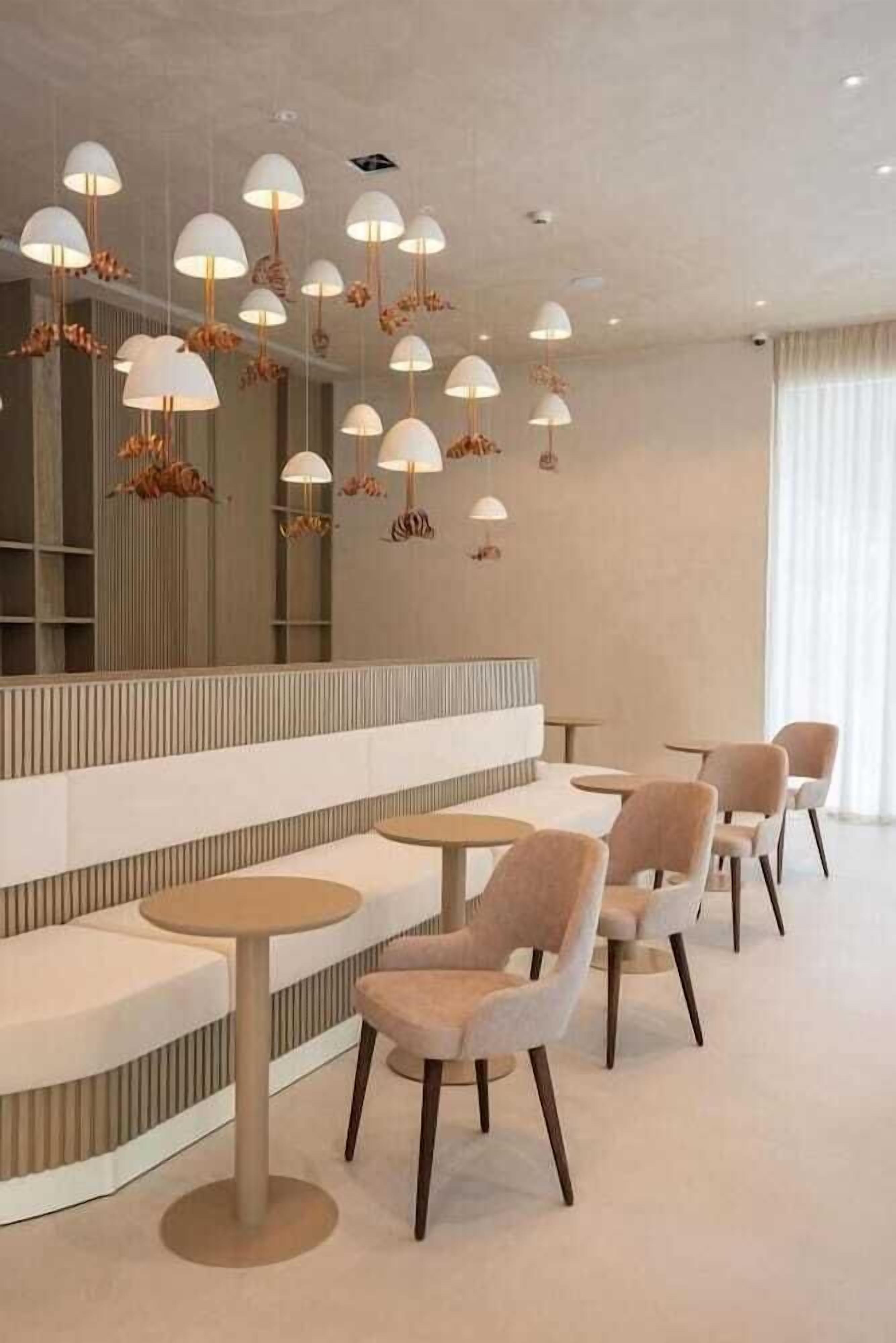 A modern interior with round tables and cushioned chairs, a long bench, and pendant lighting with floral designs.